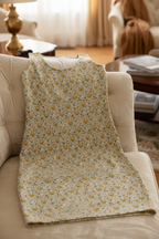 Floral-patterned blanket draped over a beige armchair in a living room setting.