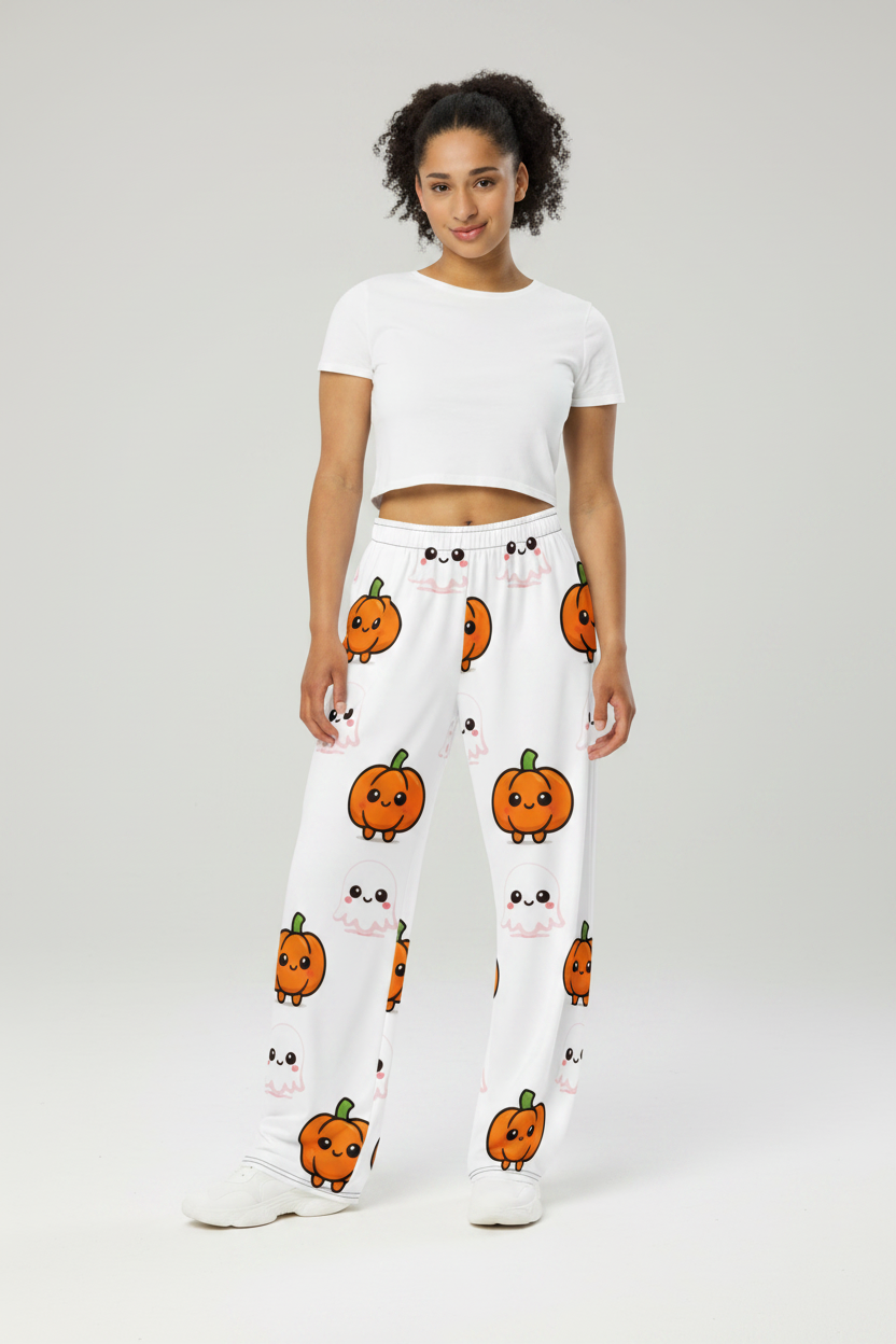 A model stands against a light gray studio background wearing white sweatpants with a repeating orange pumpkin face pattern and a white cropped short-sleeve top.