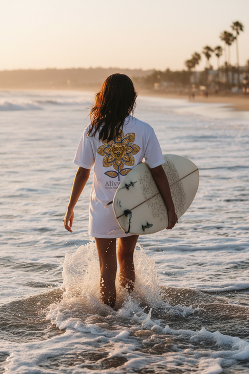 Person holding a surfboard walking into the ocean at sunset