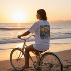 Woman riding a bicycle on a beach at sunset with a colorful shirt.