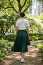 Person wearing a white t-shirt and green pleated skirt walking in a park.