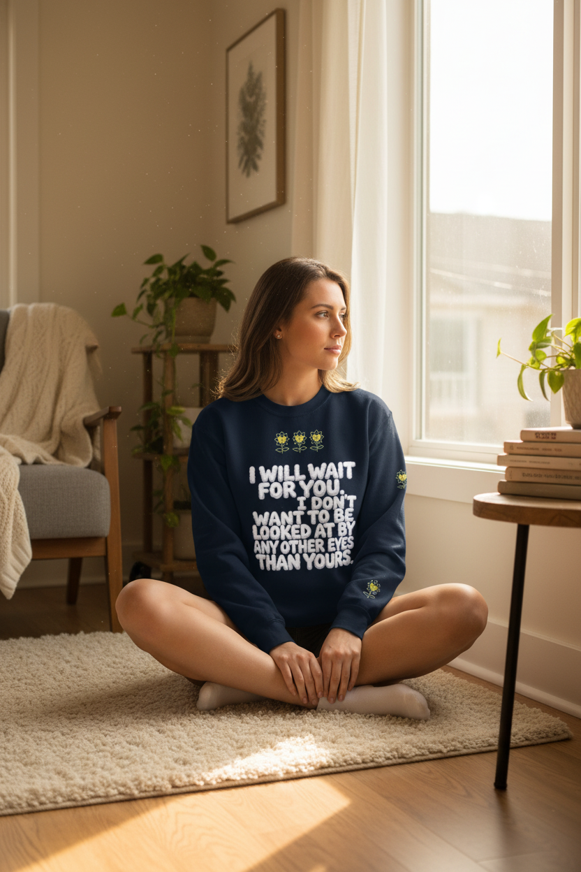 Woman sitting on the floor wearing a blue sweatshirt with text in a sunlit room.