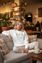 Woman sitting on a couch in a cozy cafe wearing a white sweatshirt with floral designs.