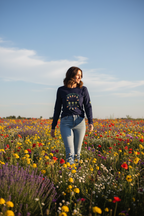 Woman walking through a field of wildflowers with a clear blue sky.
