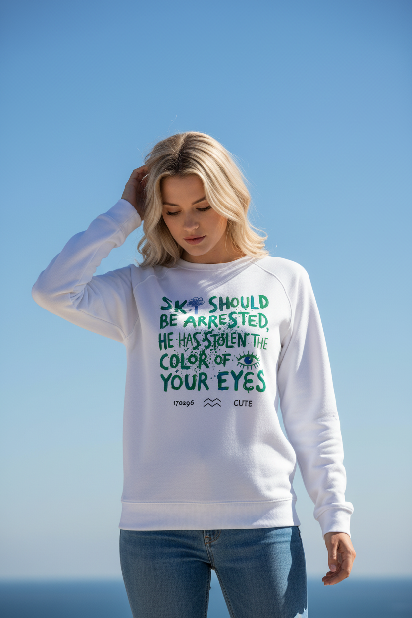 A woman wearing a white crewneck sweatshirt with a green graphic text print that reads 'SKY SHOULD BE ARRESTED, HE HAS STOLEN THE COLOR OF YOUR EYES' and 'rough CUTE' underneath, set against a clear blue sky background.