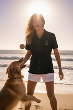 Woman in a black polo shirt and white shorts playing with a dog on a beach.