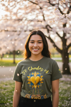 Woman wearing a green t-shirt with a colorful design in front of cherry blossom trees
