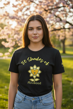 Person wearing a black t-shirt with a yellow graphic and text, standing outdoors in a park.