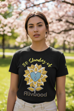Woman wearing a black t-shirt with a sunflower design and '50 Shades of Alivwood' text in a park with cherry blossoms.