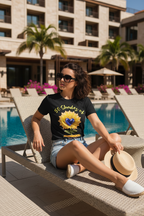 Woman sitting by a pool wearing a black t-shirt with a colorful design, sunglasses, and denim shorts.