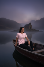 Woman in a pink shirt sitting in a rowboat on a misty lake with a church in the background.