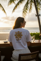 Person wearing a white t-shirt with a floral design and 'Allwood' branding, sitting at a table with palm trees and sunset in the background.