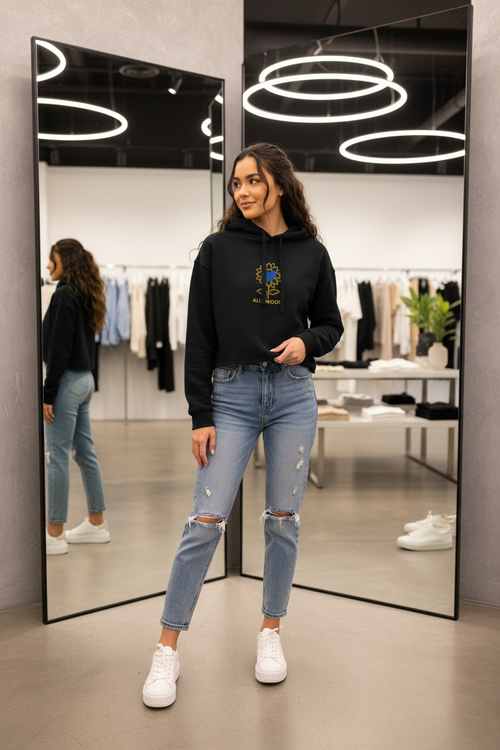 Woman in a black hoodie and ripped jeans standing in front of a mirror in a store.